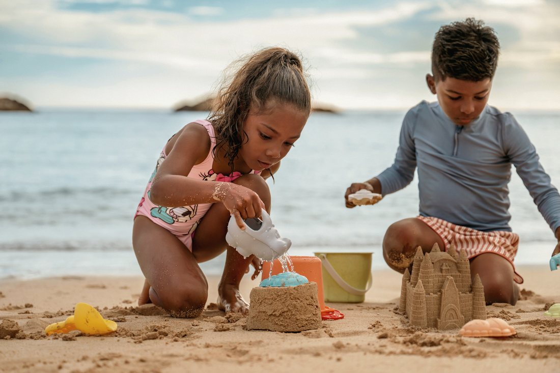 Two children building sandcastles on the beach at AULANI Resort.