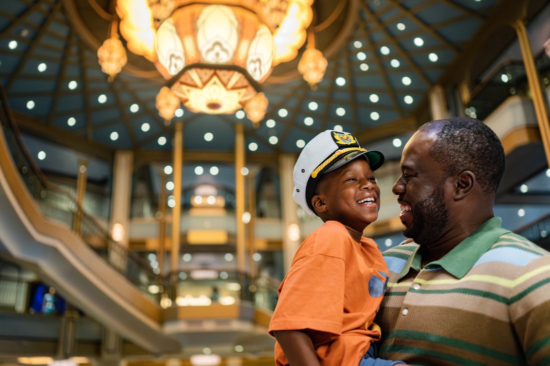 A father and son in captain hats laughing together on board the Disney Treasure.