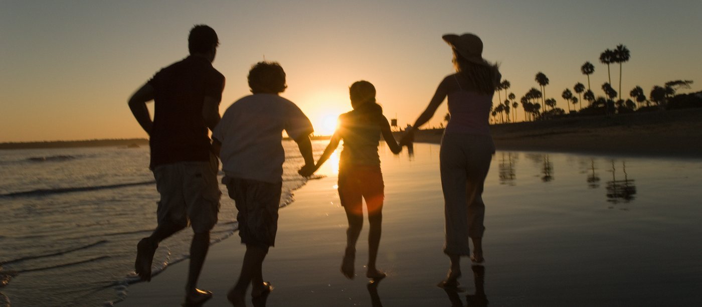 A family running hand in hand along the shoreline at sunset.