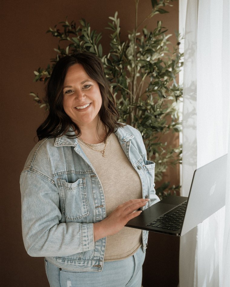 Cydnie in a denim jacket holding a laptop, smiling.