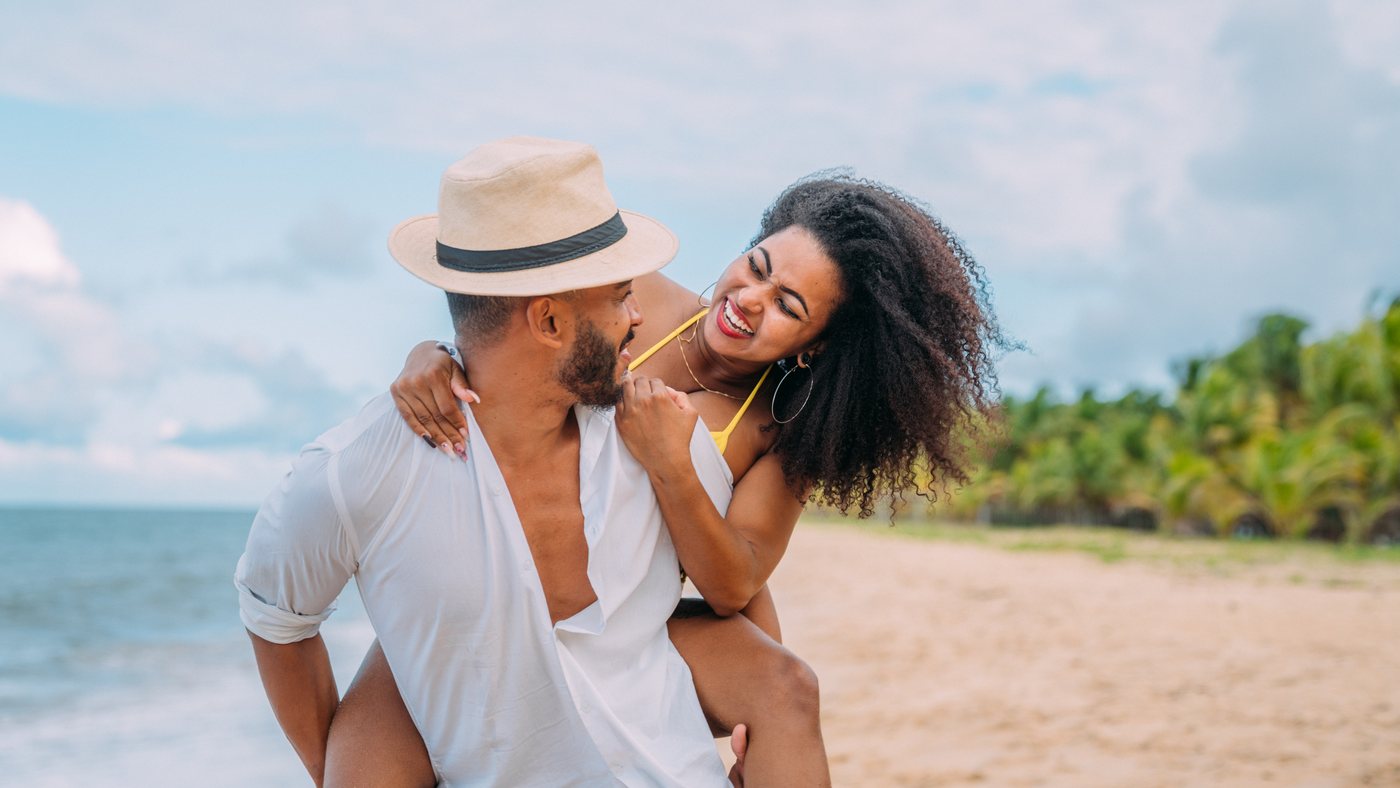 A laughing couple on a tropical beach, the man carrying the woman on his back.