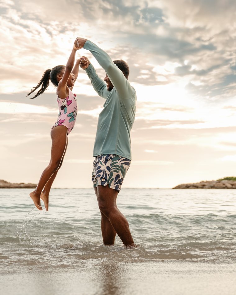 A father lifts his young daughter in the shallow lagoon at sunset at AULANI Resort.