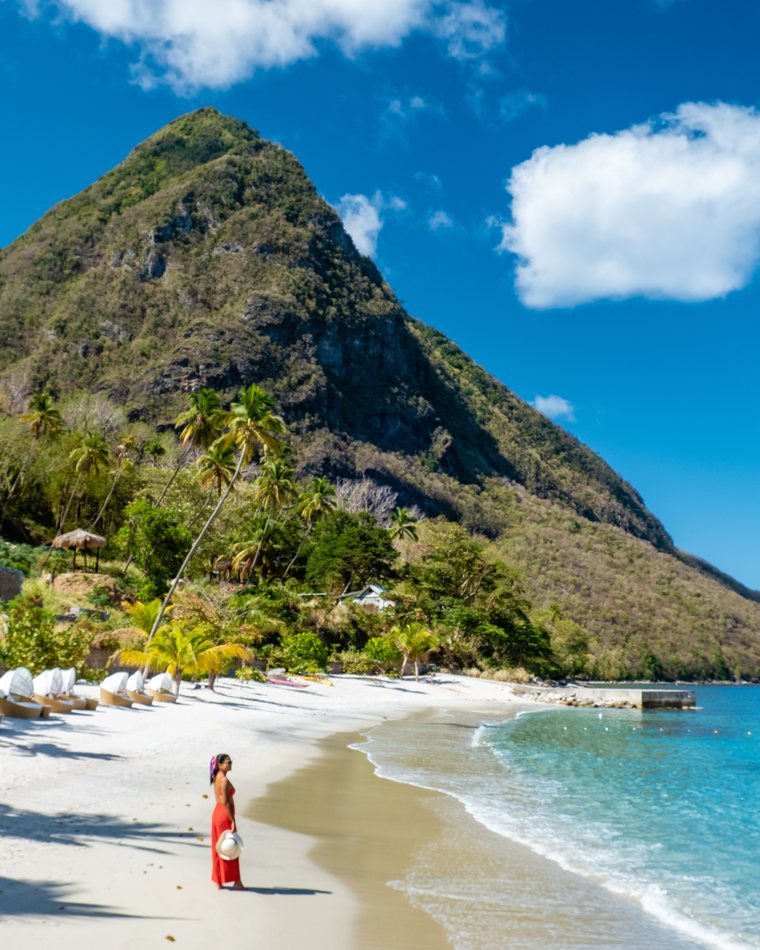 A woman in a red dress on a white sand beach below Petit Piton.