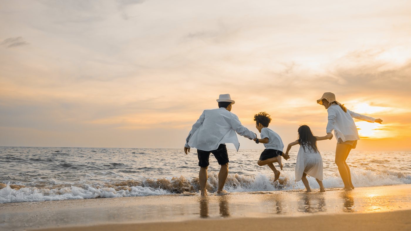 A family running hand in hand into the surf at golden hour.