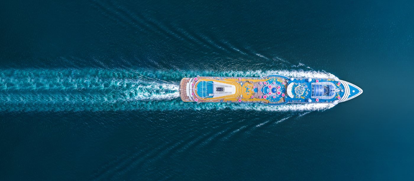 A cruise ship seen from above, trailing a wake across turquoise water.