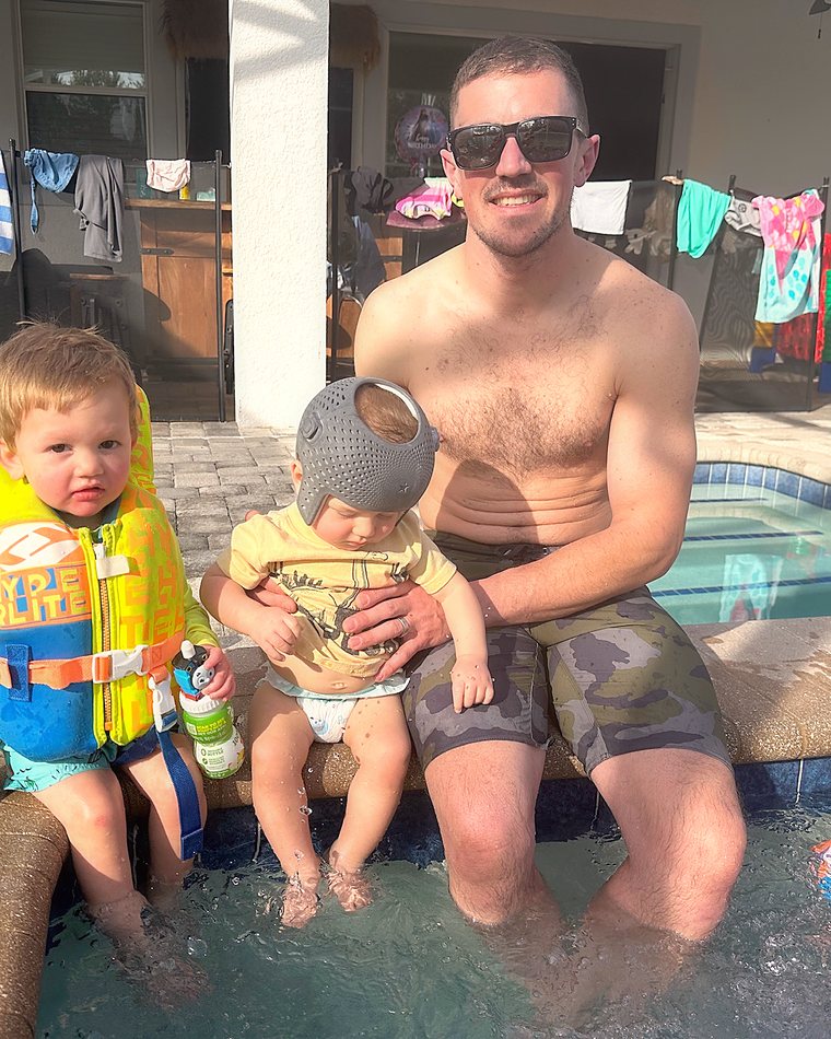 Cydnie's husband sitting on a pool edge with their two boys.