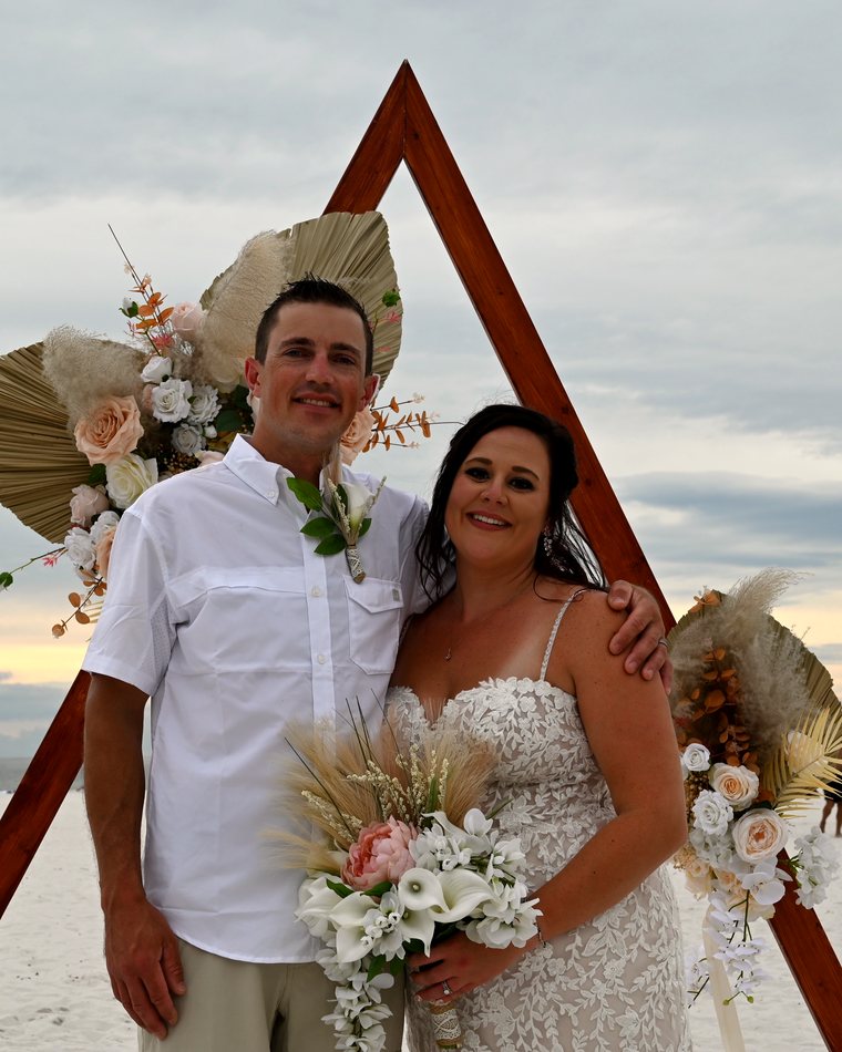 Cydnie and her husband in front of their wooden wedding arch on the beach.